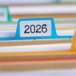 Close-up de um arquivo físico com divisórias coloridas, destacando uma aba azul identificada com o ano “2026”. Pastas e documentos organizados aparecem desfocados ao fundo, representando arquivamento, gestão documental, organização de processos e controle de registros. Logotipo da empresa visível no canto superior esquerdo.